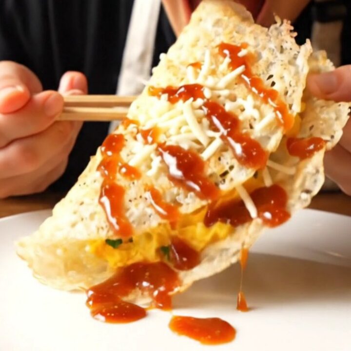 A close-up of a golden, blistered rice paper crepe filled with fluffy eggs and melted cheese.