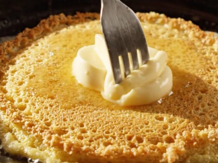 Crispy golden cornmeal pancakes stacked with a dollop of melting honey butter on top.
