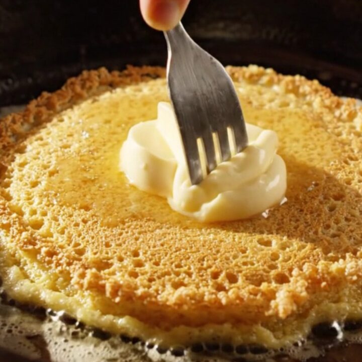 Crispy golden cornmeal pancakes stacked with a dollop of melting honey butter on top.