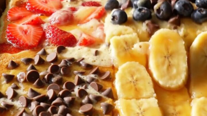 A golden, fluffy sheet pan pancake divided into four distinct quadrants featuring strawberries, blueberries, chocolate