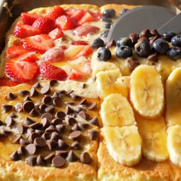 A golden, fluffy sheet pan pancake divided into four distinct quadrants featuring strawberries, blueberries, chocolate