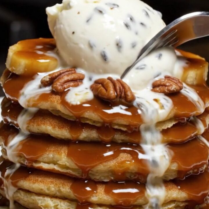 A stack of fluffy pancakes topped with caramelized bananas, toasted pecans, and a melting scoop of mascarpone.