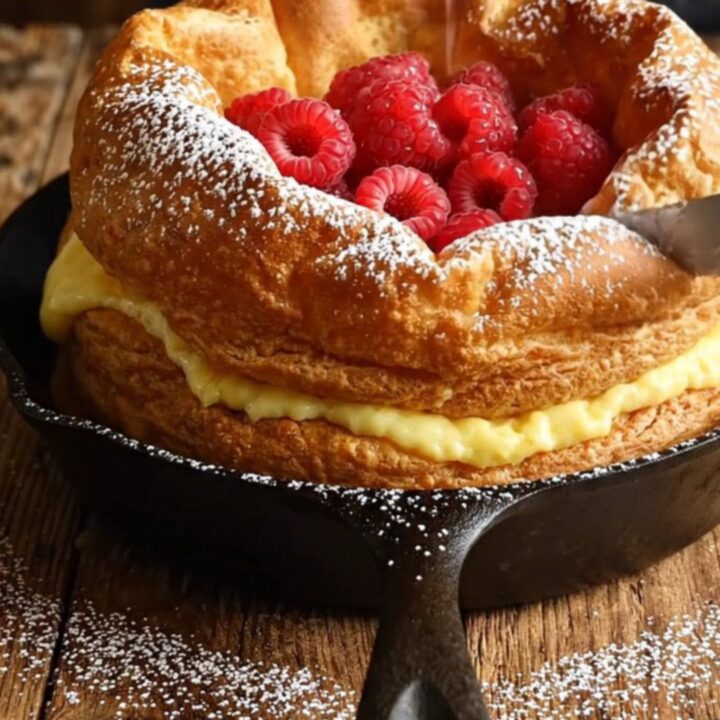 A towering, golden-brown Dutch baby pancake with crispy ruffled edges served in a cast-iron skillet.