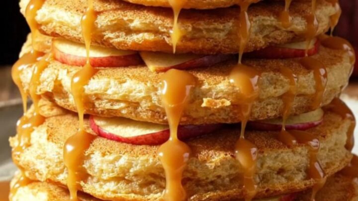 A stack of golden-brown apple cider pancake rings topped with caramel and walnuts.
