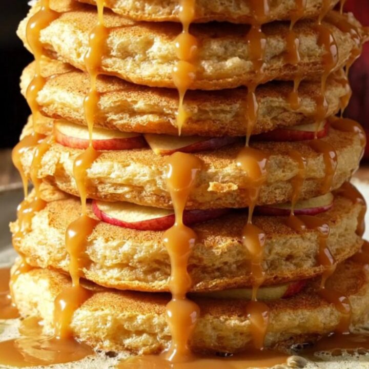 A stack of golden-brown apple cider pancake rings topped with caramel and walnuts.
