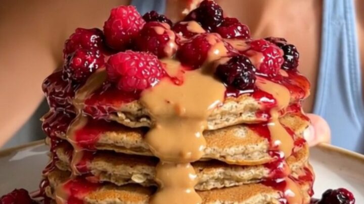 A tall stack of golden brown blender pancakes topped with bubbling berry compote and almond butter.