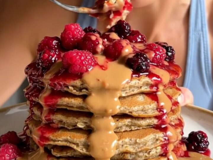 A tall stack of golden brown blender pancakes topped with bubbling berry compote and almond butter.