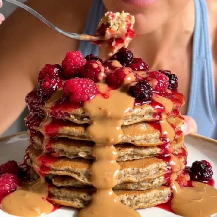 A tall stack of golden brown blender pancakes topped with bubbling berry compote and almond butter.