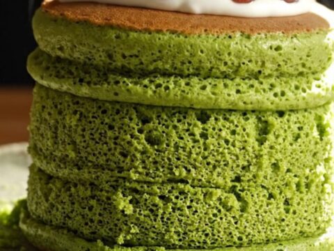 Two emerald matcha soufflé pancakes topped with sweet red beans and cream.