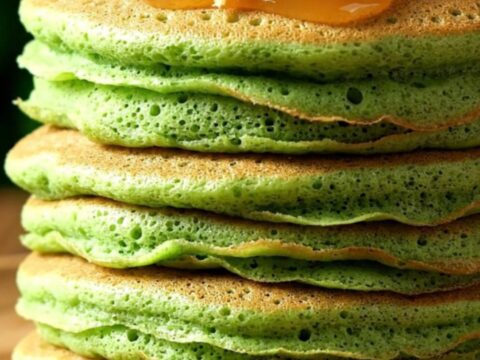A stack of vibrant jade-green pandan pancakes drizzled with glossy amber kaya coconut jam and sprinkled with toasted coconut.