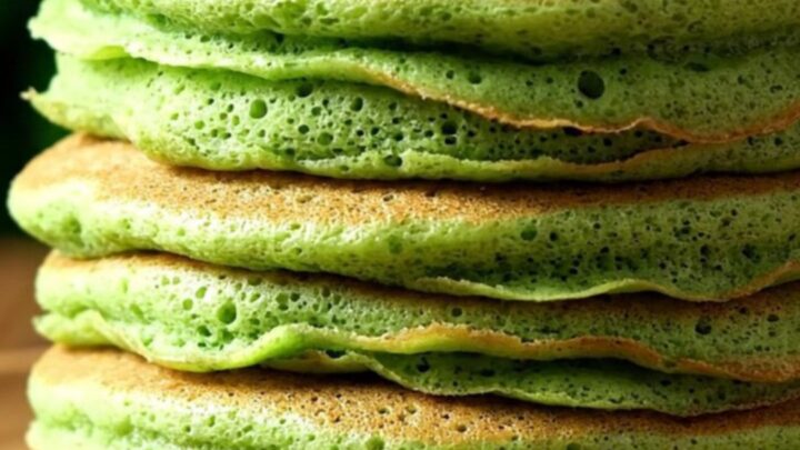 A stack of vibrant jade-green pandan pancakes drizzled with glossy amber kaya coconut jam and sprinkled with toasted coconut.