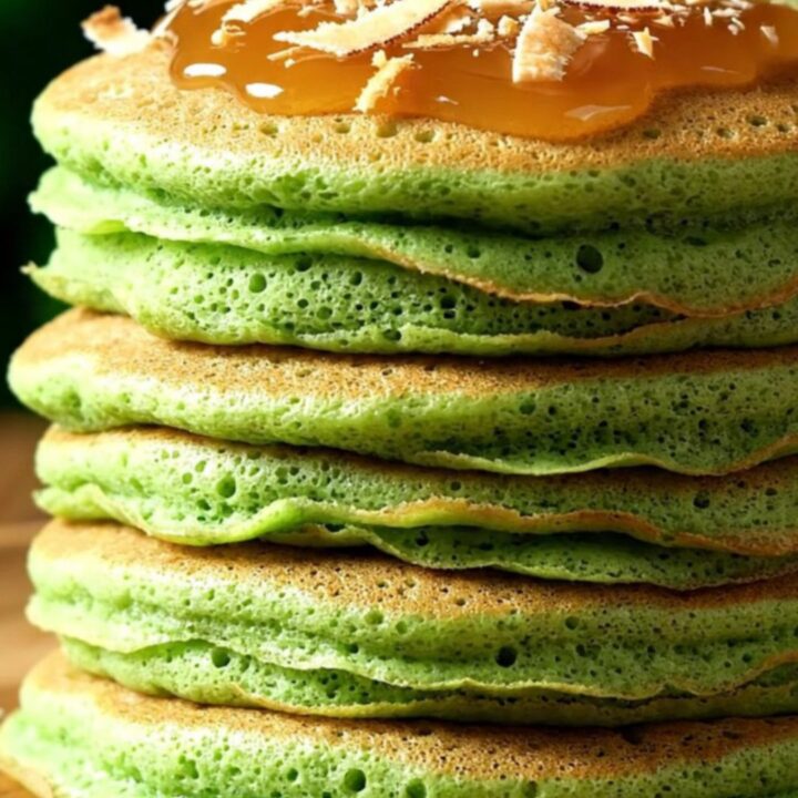 A stack of vibrant jade-green pandan pancakes drizzled with glossy amber kaya coconut jam and sprinkled with toasted coconut.