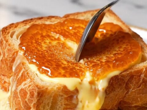 A close-up of a thick slice of golden-brown French toast topped with a perfectly caramelized, amber-colored sugar crust.