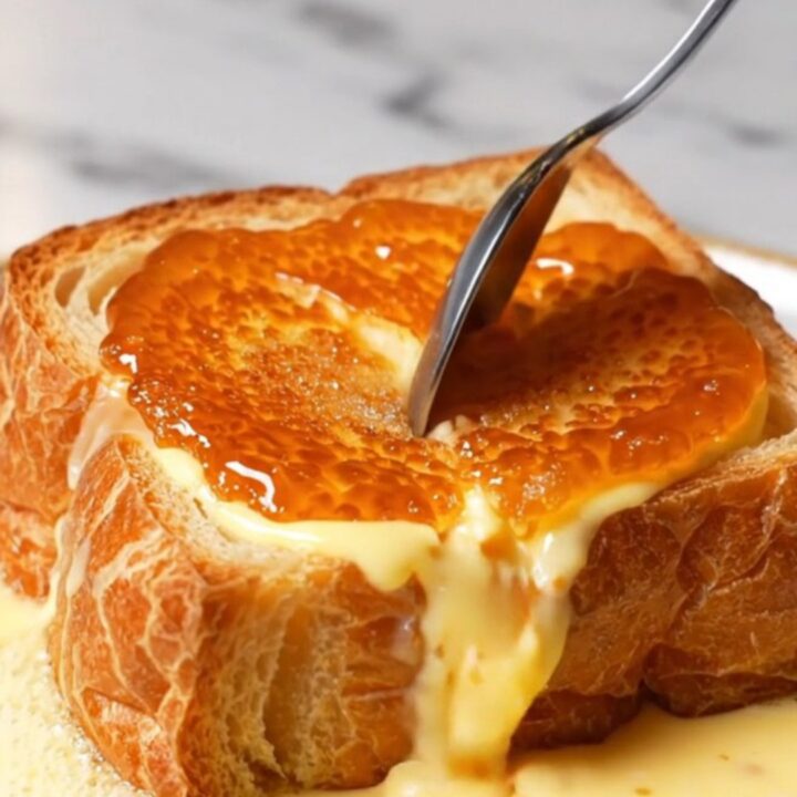 A close-up of a thick slice of golden-brown French toast topped with a perfectly caramelized, amber-colored sugar crust.