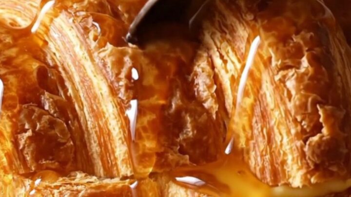 A warm, golden brown croissant French toast casserole in a ceramic dish, topped with caramelized pecans.