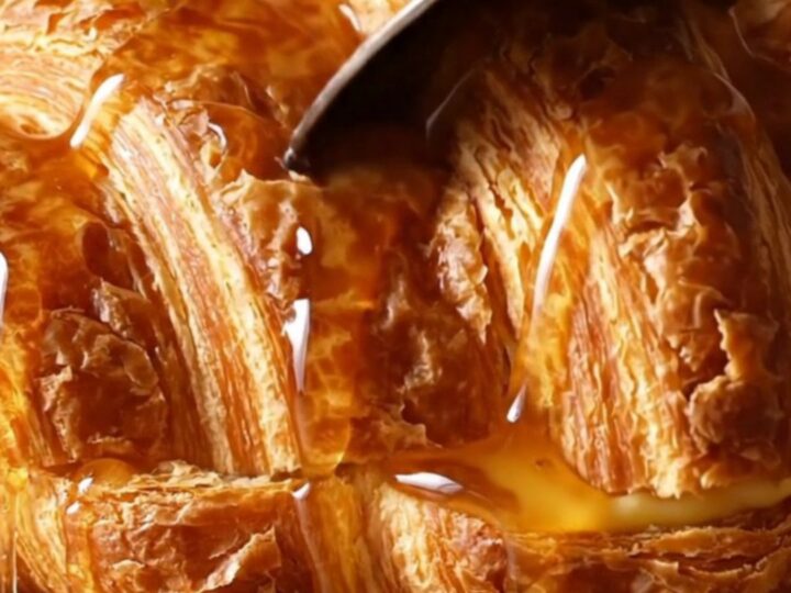 A warm, golden brown croissant French toast casserole in a ceramic dish, topped with caramelized pecans.