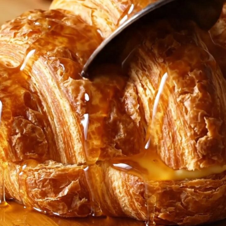 A warm, golden brown croissant French toast casserole in a ceramic dish, topped with caramelized pecans.