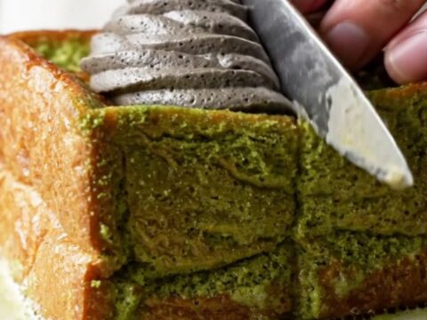 A thick square of matcha French toast with golden edges, topped with a dramatic swirl of black sesame whipped cream.
