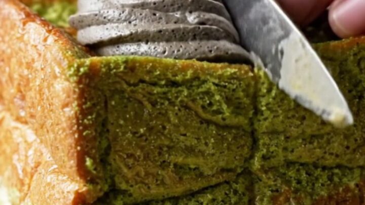 A thick square of matcha French toast with golden edges, topped with a dramatic swirl of black sesame whipped cream.
