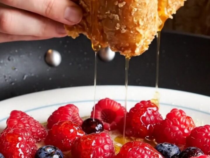 A close-up of golden-brown cornflake-crusted French toast topped with fresh berries and maple syrup.