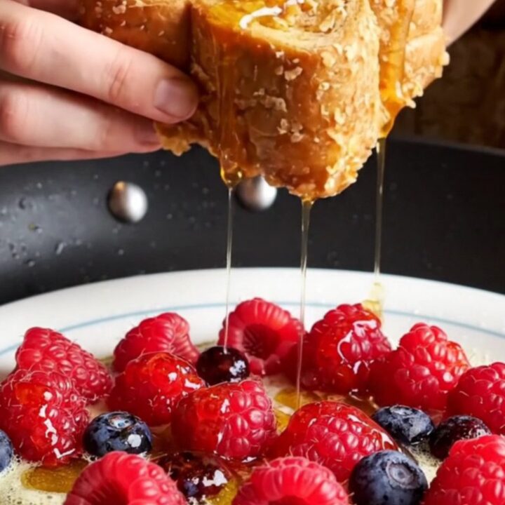A close-up of golden-brown cornflake-crusted French toast topped with fresh berries and maple syrup.