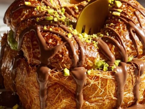 A stack of golden brown brioche French toast topped with a drizzle of melted milk chocolate and crushed pistachios.