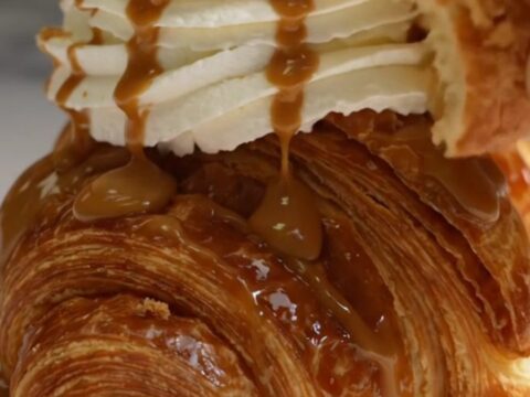 A golden-brown, caramelized croffle topped with whipped cream, cookie butter drizzle, and biscuit crumbs.