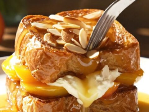 A close-up view of golden-brown stuffed brioche topped with glossy, bourbon-caramelized peach slices.