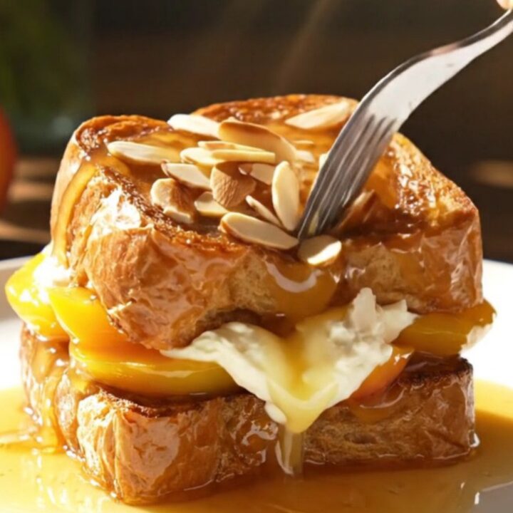 A close-up view of golden-brown stuffed brioche topped with glossy, bourbon-caramelized peach slices.