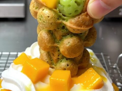 A golden-green pandan bubble waffle cone filled with whipped coconut cream and fresh diced mango.