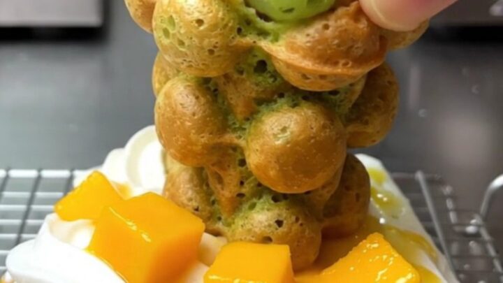 A golden-green pandan bubble waffle cone filled with whipped coconut cream and fresh diced mango.