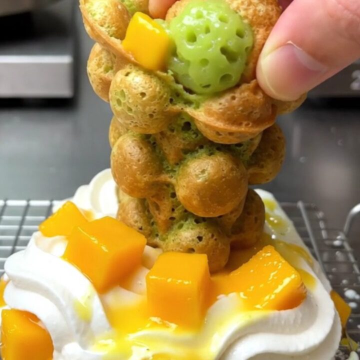 A golden-green pandan bubble waffle cone filled with whipped coconut cream and fresh diced mango.