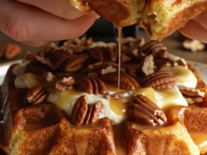 A close-up of a golden-brown Belgian waffle topped with cream and pecan pieces.