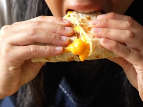 A crispy, golden-brown four-quadrant breakfast tortilla sliced in half to show molten cheese, bacon, and fluffy eggs.