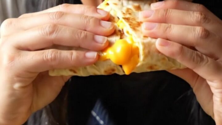 A crispy, golden-brown four-quadrant breakfast tortilla sliced in half to show molten cheese, bacon, and fluffy eggs.
