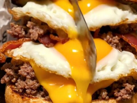 A close-up of a cut everything bagel sandwich showing melted cheese, seasoned ground beef, and a runny egg yolk.