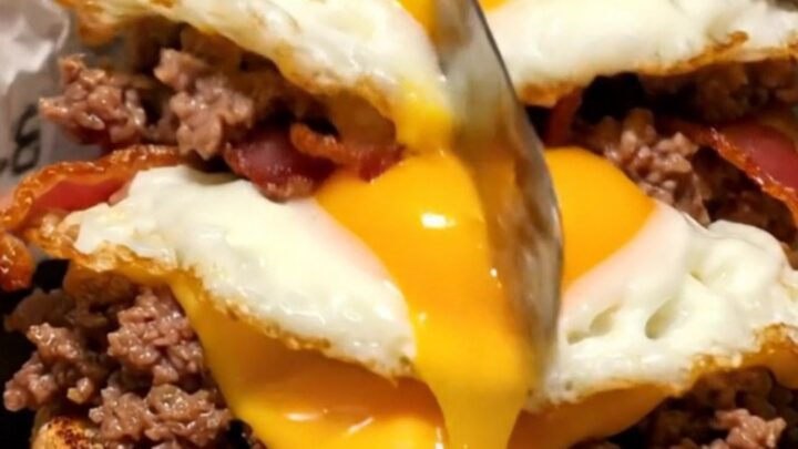 A close-up of a cut everything bagel sandwich showing melted cheese, seasoned ground beef, and a runny egg yolk.