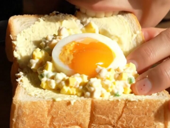 A close-up view of a perfectly cut Tamago Sando showing a jammy egg center and creamy egg salad.