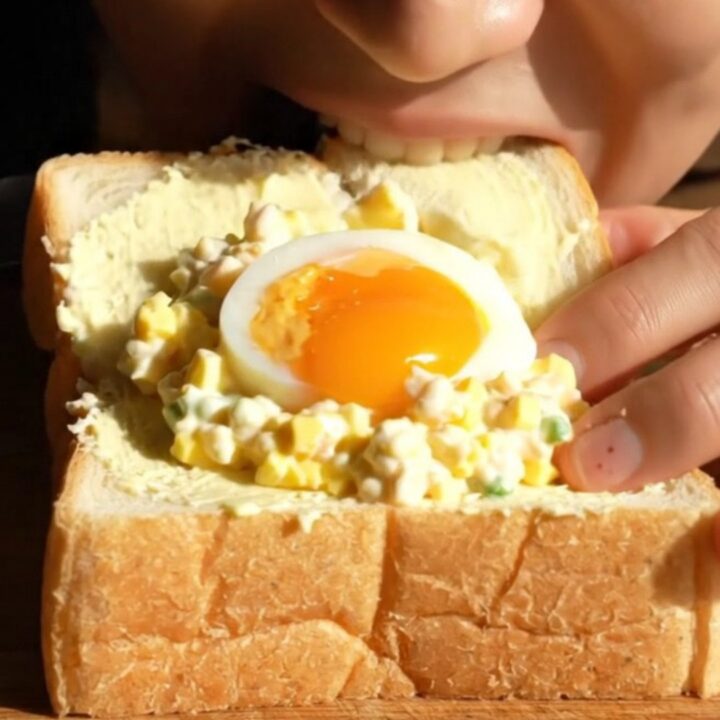A close-up view of a perfectly cut Tamago Sando showing a jammy egg center and creamy egg salad.
