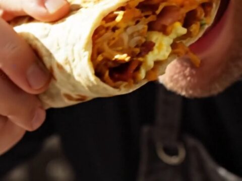 A sliced California breakfast burrito showing layers of hashbrowns, eggs, bacon, cheese, and guacamole.