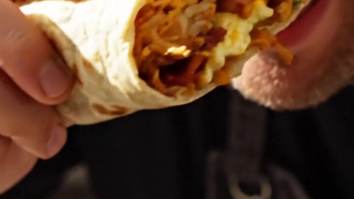 A sliced California breakfast burrito showing layers of hashbrowns, eggs, bacon, cheese, and guacamole.
