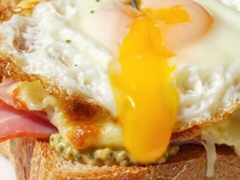 A golden-broiled Croque Madame topped with a sunny-side up egg on a marble bistro table.