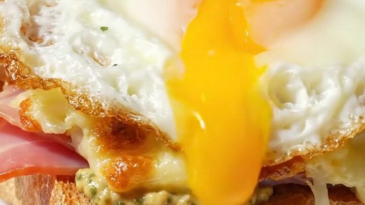 A golden-broiled Croque Madame topped with a sunny-side up egg on a marble bistro table.