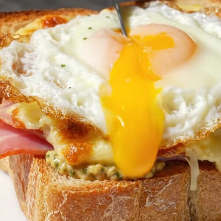 A golden-broiled Croque Madame topped with a sunny-side up egg on a marble bistro table.