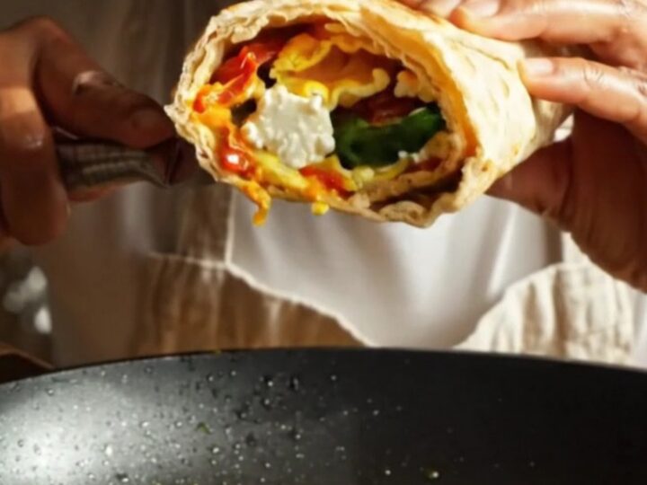 A close-up shot of a crispy, golden-seared lavash wrap sliced in half, revealing layers of fluffy egg whites, wilted spinach