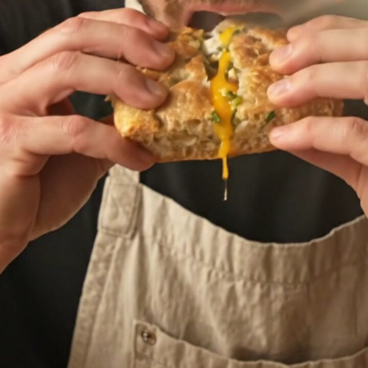 A close-up of a crispy rosemary focaccia breakfast panini showing layers of burrata, pesto, prosciutto, and a runny egg yolk.