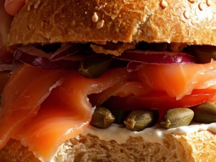 A close-up of a toasted everything bagel topped with creamy scallion-dill schmear, silky Nova lox, and fresh tomato slices.