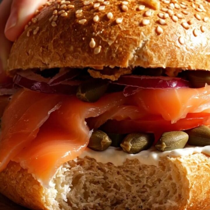A close-up of a toasted everything bagel topped with creamy scallion-dill schmear, silky Nova lox, and fresh tomato slices.
