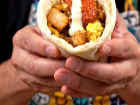 A close-up of a grilled chicken and rice breakfast wrap with scrambled eggs and garlic sauce.