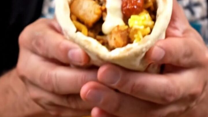 A close-up of a grilled chicken and rice breakfast wrap with scrambled eggs and garlic sauce.